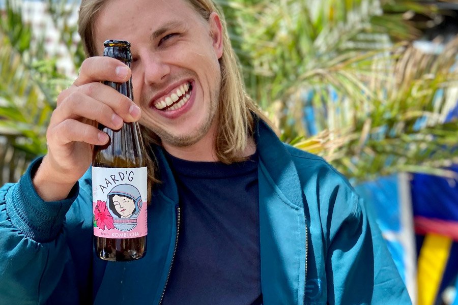 Een van de oprichters van Aard'g, Zeger, lachend met een flesje Aard'g Bloem Kombucha in zijn hand.